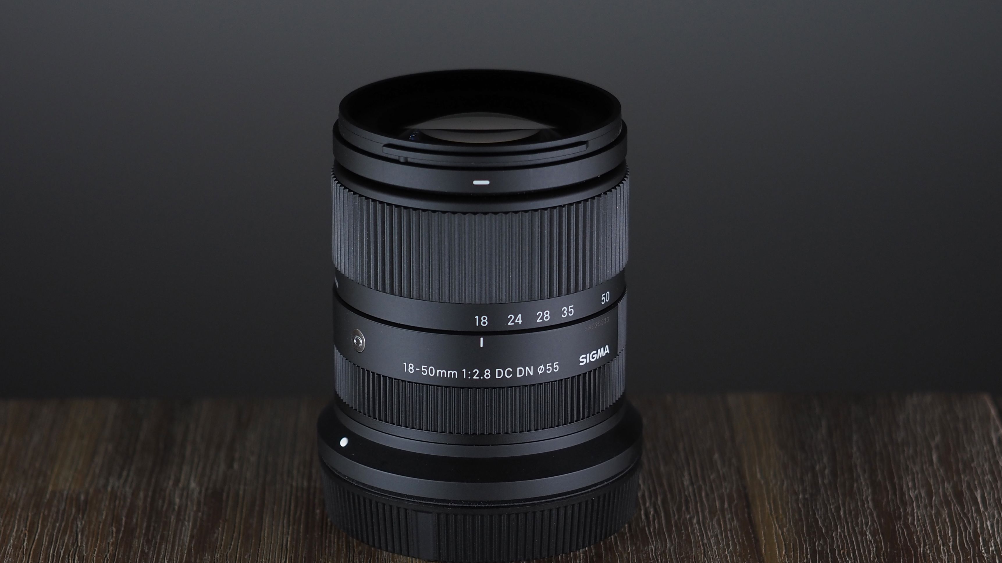 The Sigma 18-50mm f/2.8 DC DN | C Canon RF lens on a wooden surface against a dark background with moody lighting