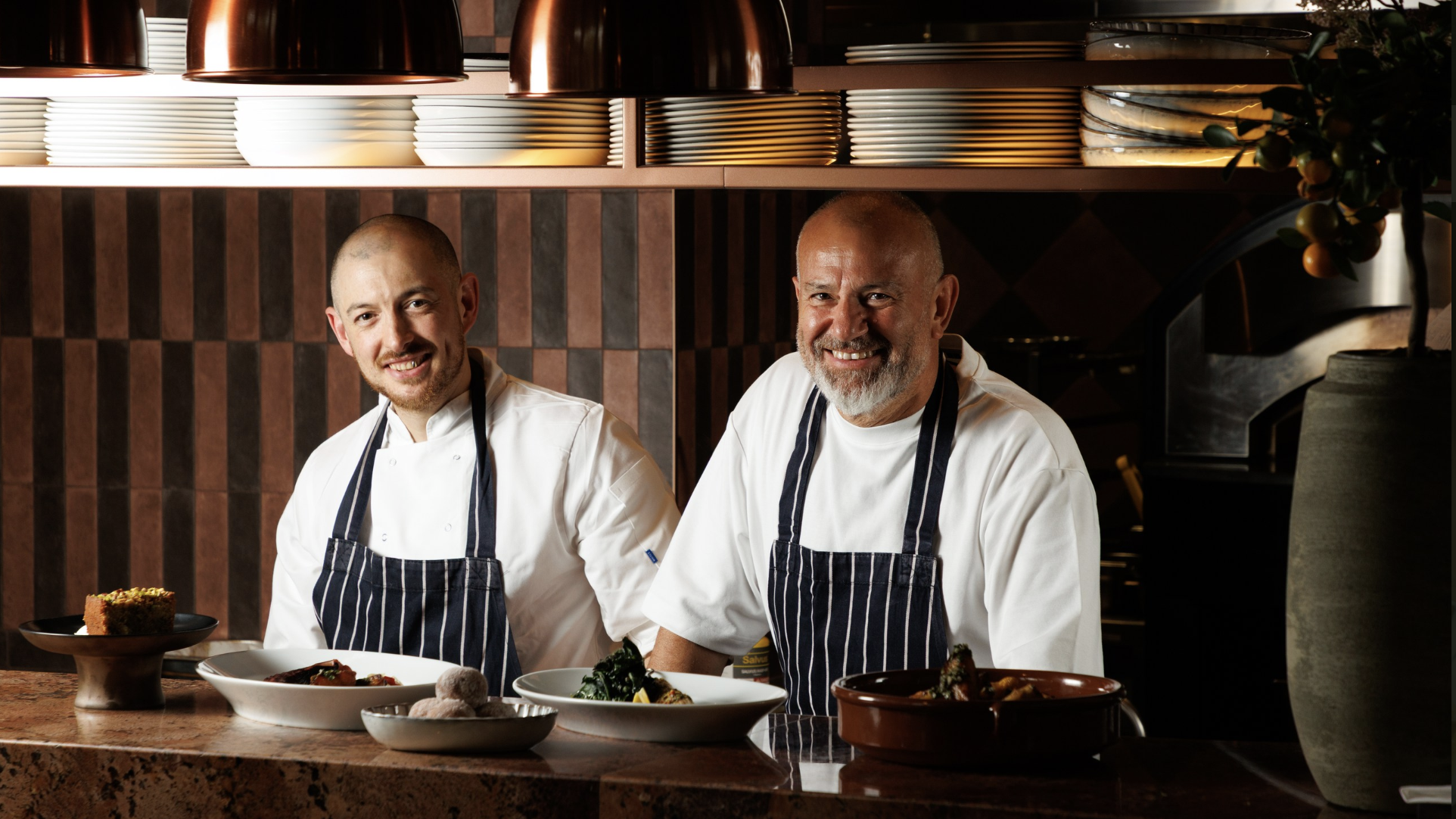 An image of two chefs at the kitchen pass with five plates of food ready to serve up at the restaurant