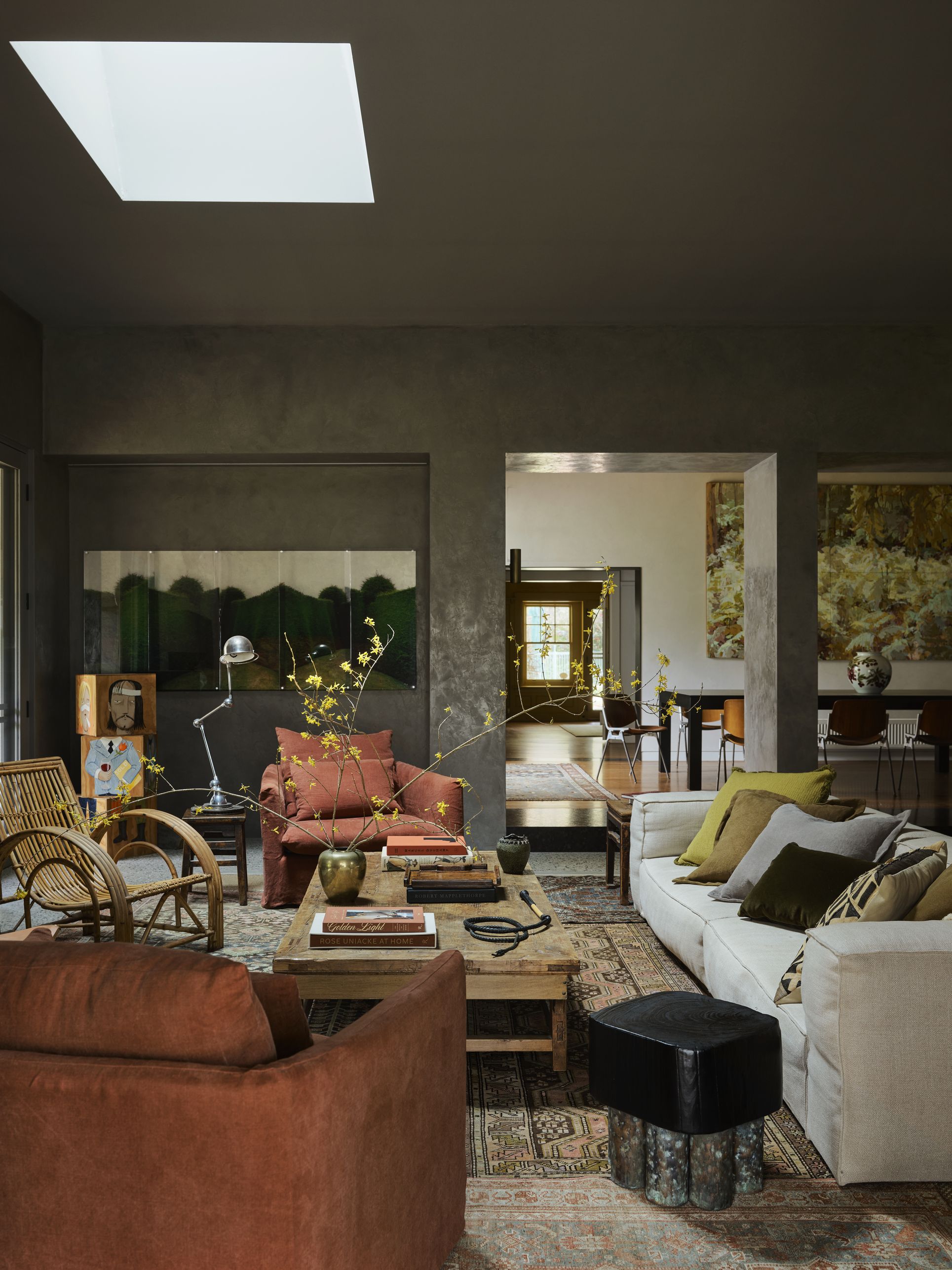 living room with textured walls, artwork, white sofa with colorful cushions, timber table styled with a vase of large stems and books, rattan chair, rust linen chair, side table with silver table lamp
