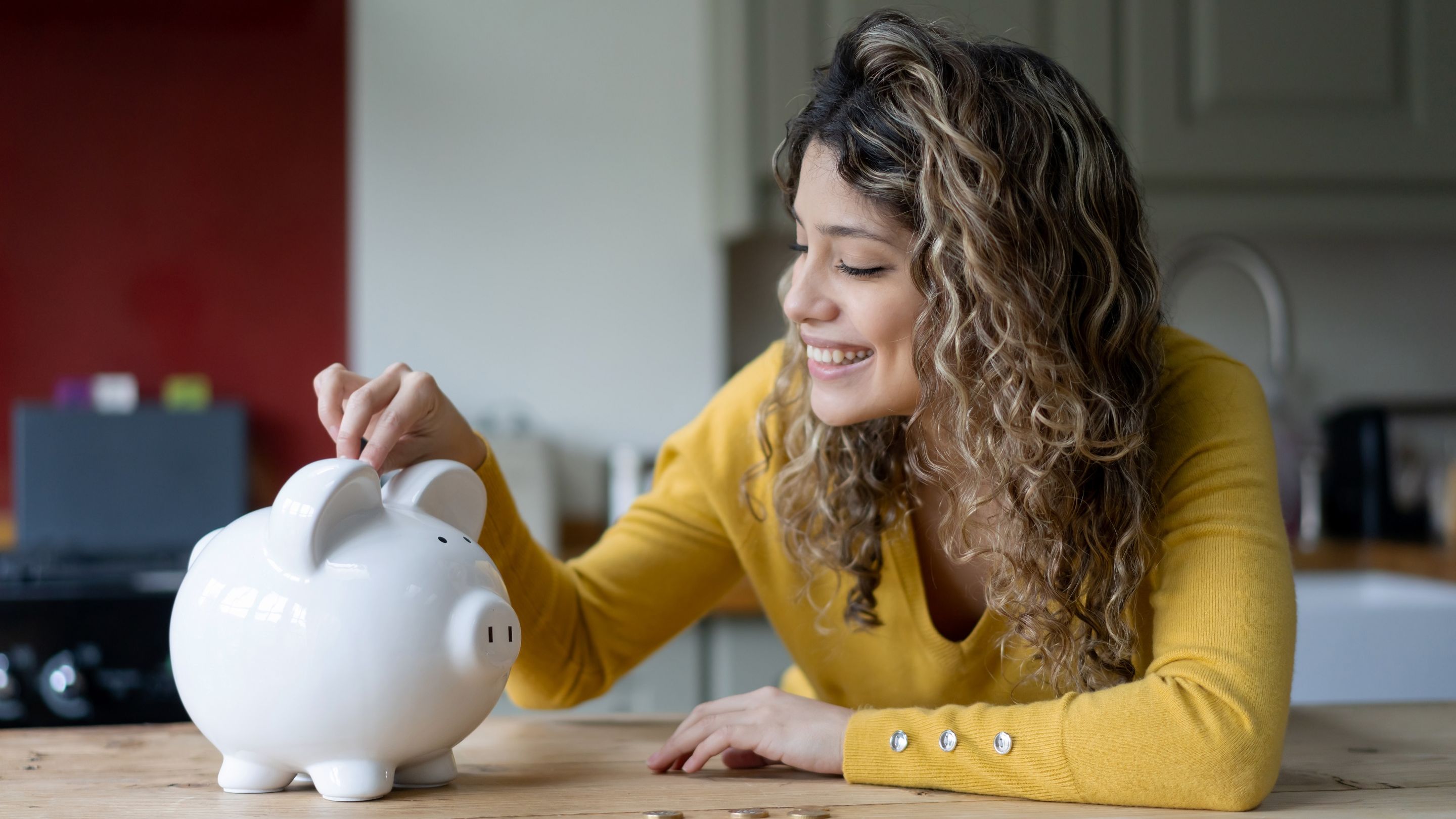 A young woman smiles as she drops a coin into a piggy bank.