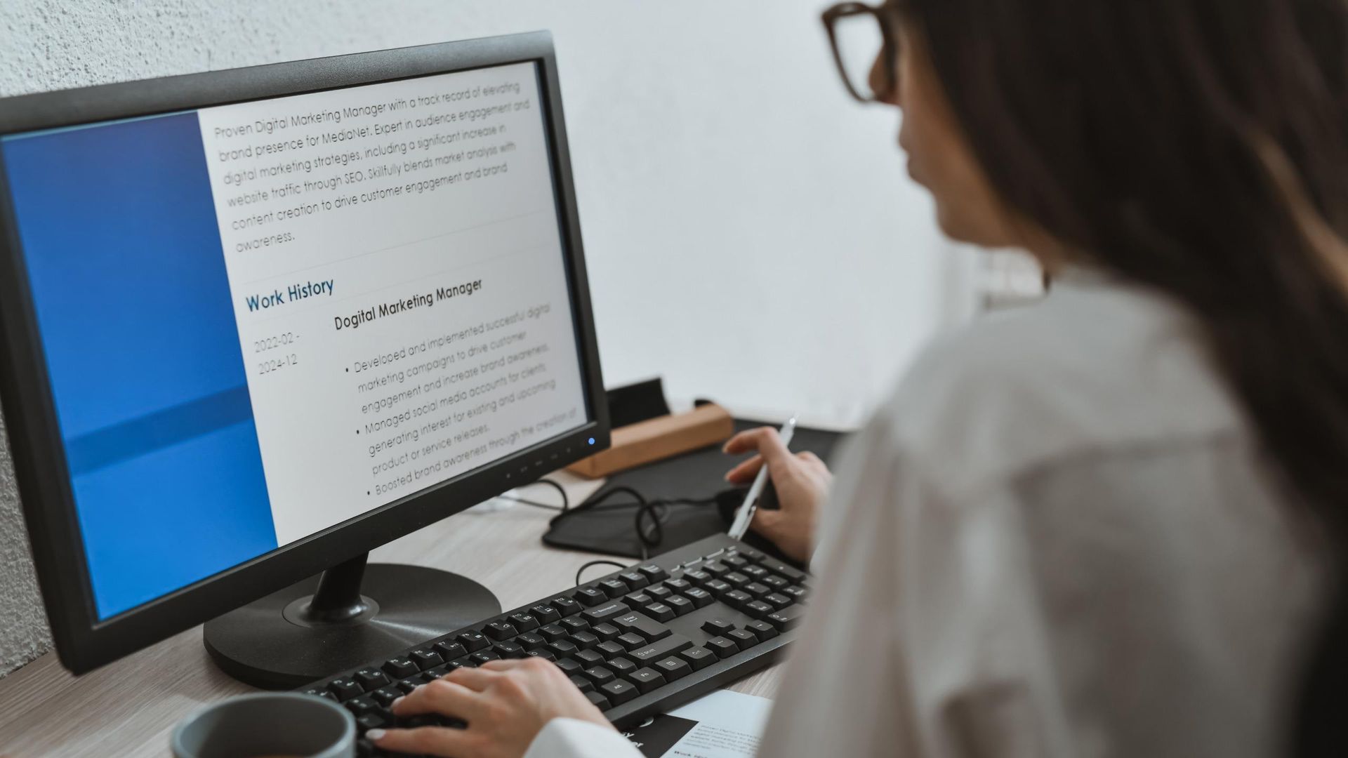 A woman with glasses edits her resume on her home computer.