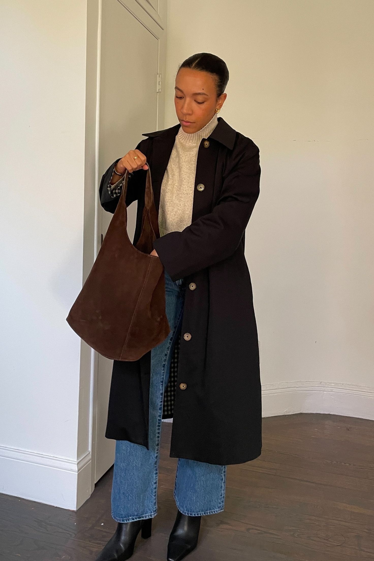 Lauren Tappan wearing a brown suede bag, a black trench coat, a beige sweater, jeans, and boots