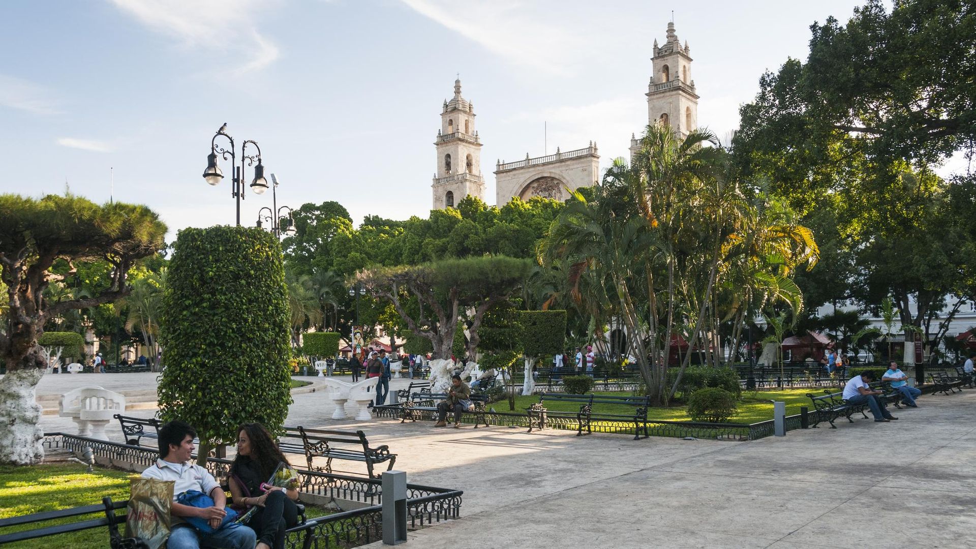 A pleasant day with people sitting on benches at the Plaza de la Independencia and Cathedral San Ildefonso in Mexico.