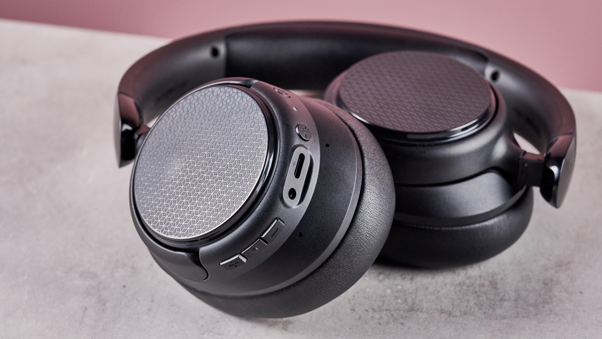 Amazon Basics Hybrid Active Noise Cancelling Headphones on a gray surface, with a pink background showing the controls on the earcup