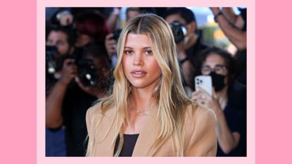 Sofia Richie pictured wearing a camel-colored coat, with a nude, glossy lip look and natural makeup on September 14, 2022 in New York City/ in a pink template