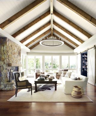 A farmhouse style living room with cream shiplap, wooden beams on ceiling and stone wall
