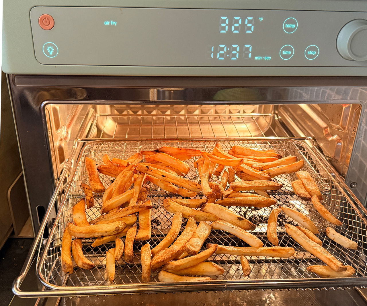 French fries on a wire tray inside a blue oven style air fryer.