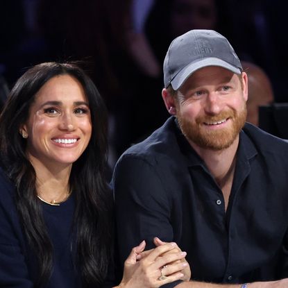 Prince Harry and Meghan Markle sitting next to each other at a basketball game and smiling