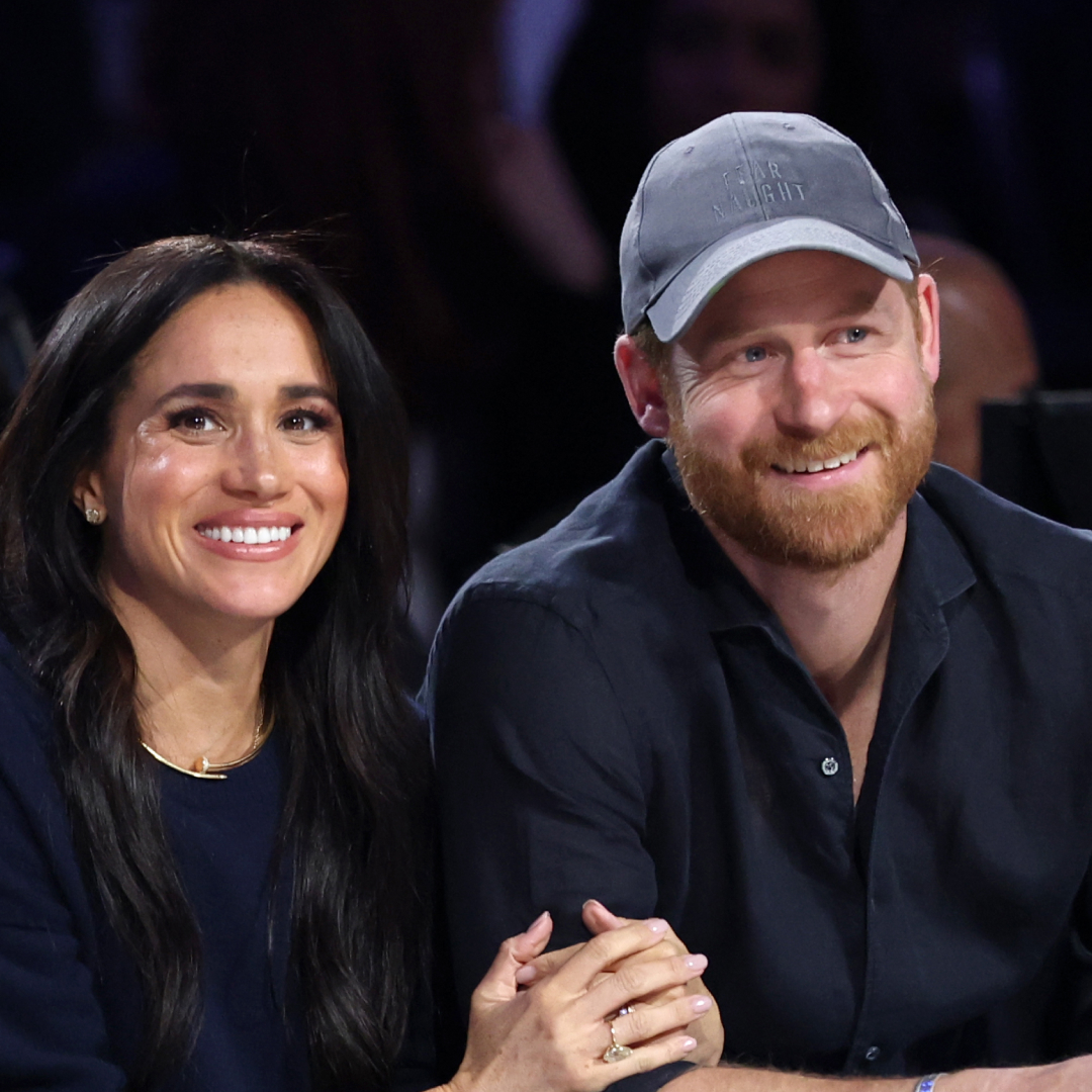 Prince Harry and Meghan Markle sitting next to each other at a basketball game and smiling