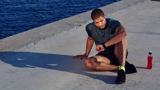 Man in workout clothing resting and checking his running watch