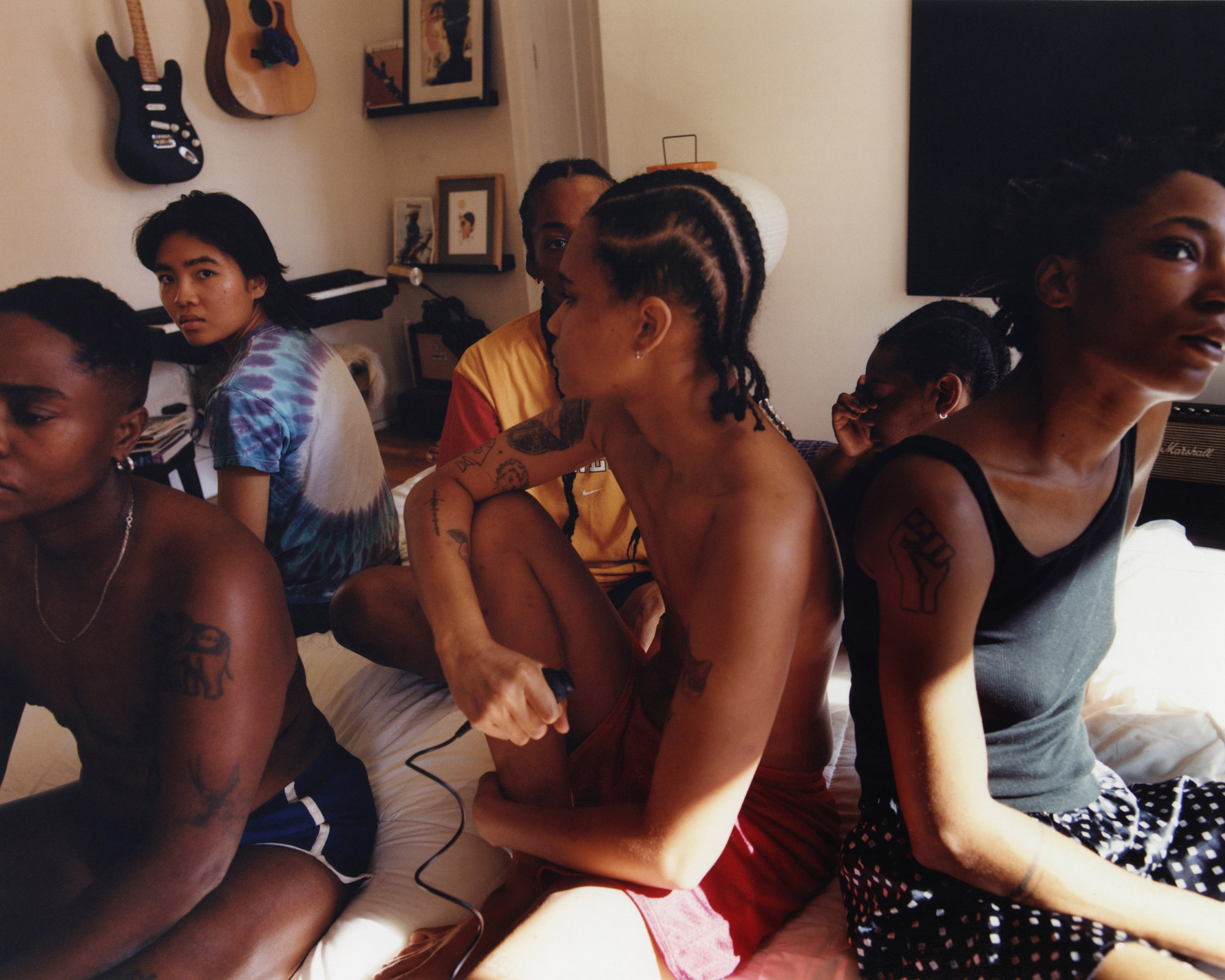 A group of young teenage girls sits on a crowded bed in summer clothes.