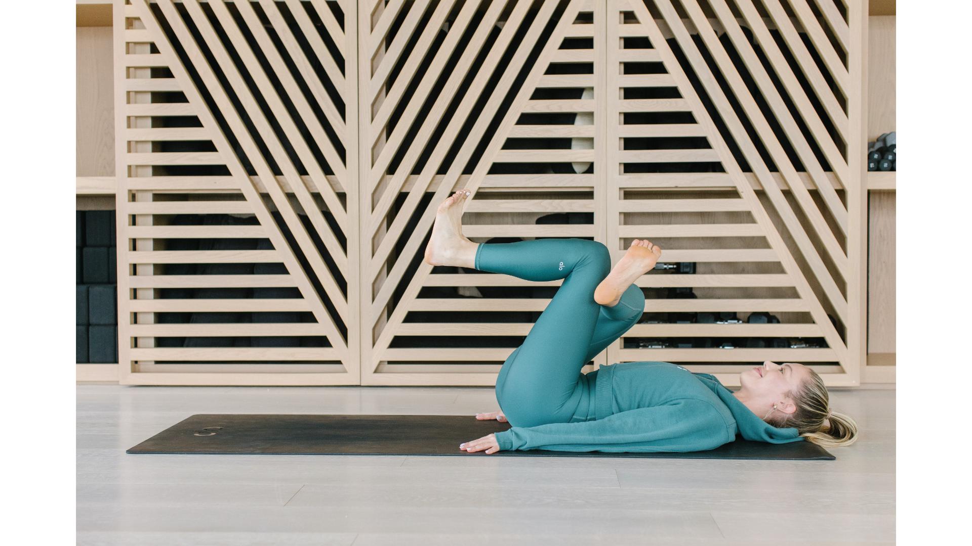 woman dressed in jade green on her back on the floor in a figure of four stretch