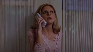 Sarah Michelle Gellar in Scream 2 talking to Ghostface on a cordless phone while looking for him nervously.