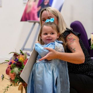 Callie Rose with her mother holding flowers and a sign for the prince and princess.