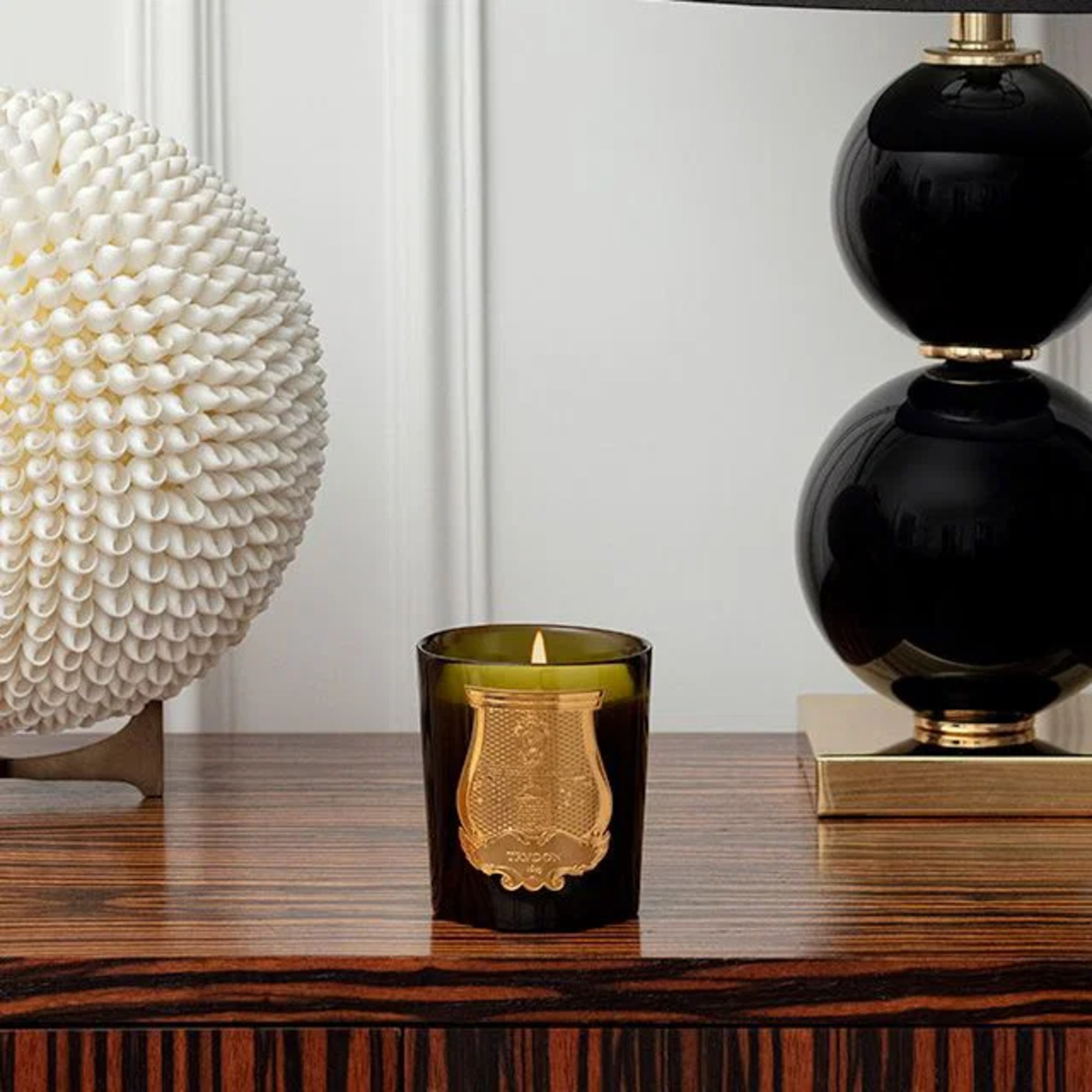 A Cire Trudon candle in a green glass jar on a sideboard with sculptural decor