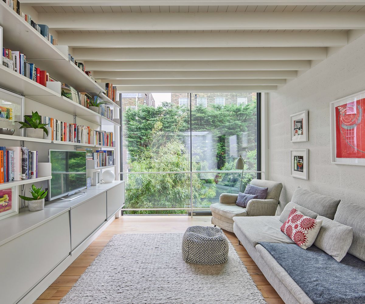 A contemporary yet cosy living area with TV and comfy light coloured sofas and built in shelving storing books and plants