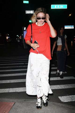 Gigi Hadid wearing a red oversized sweater, a long white maxi dress, and Adidas x Wales Bonner sneakers in New York City May 2024