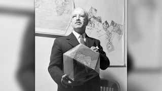 Richard Buckminster Fuller holds his assembled polyhedral globe. Note the flat map on the wall in the background.