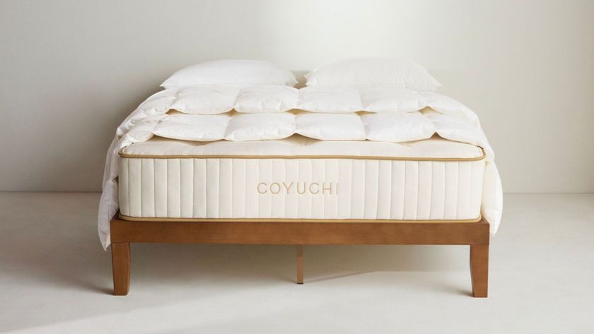 The Coyuchi Natural REM mattress on a wooden bed frame in an empty room with some bedding placed on top