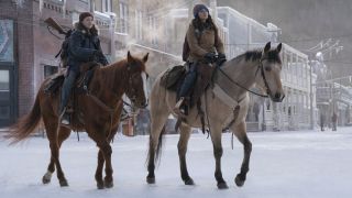 Ellie (Bella Ramsey) and Dina (Isabela Merced) ride horses through a show covered town in The Last of Us season 2