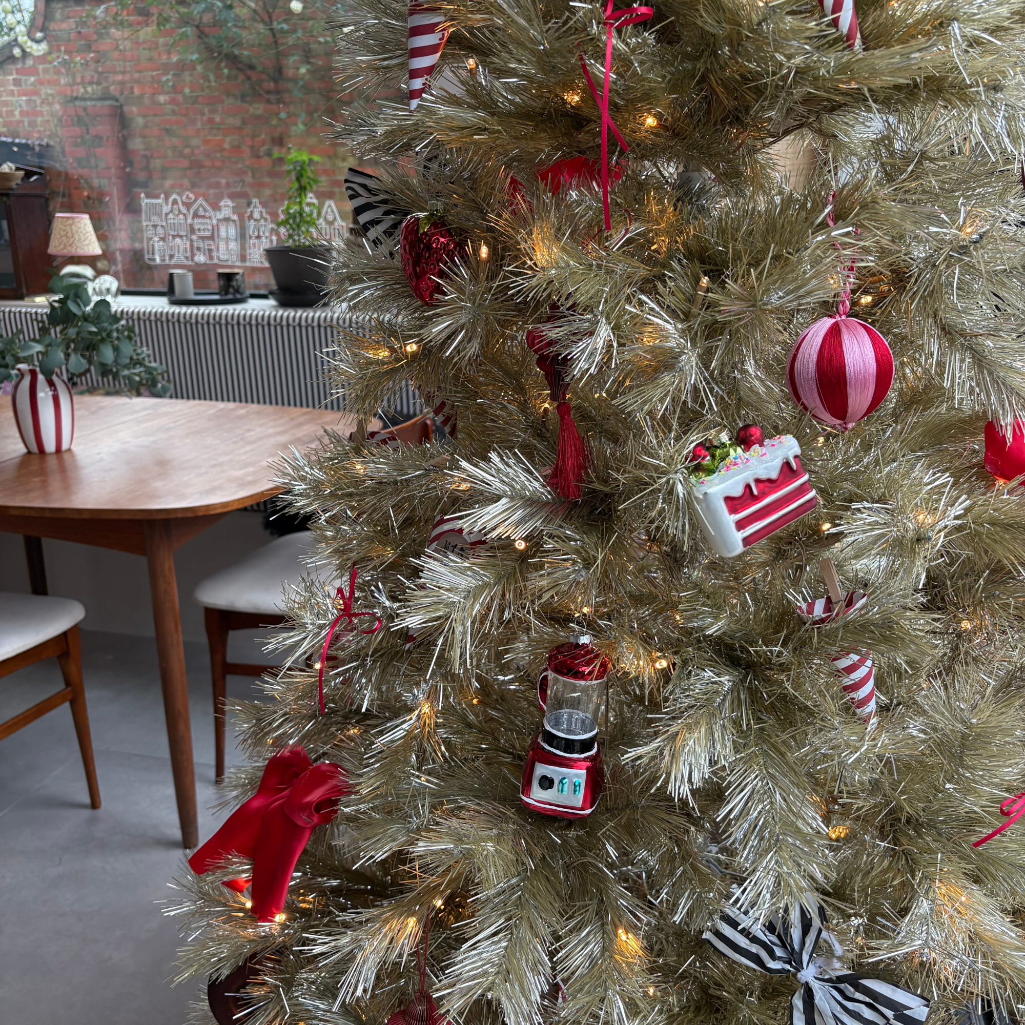 Close-up of Heather&#039;s food themed baubles on her gold tree. A slice of cake bauble and blender bauble are in view.