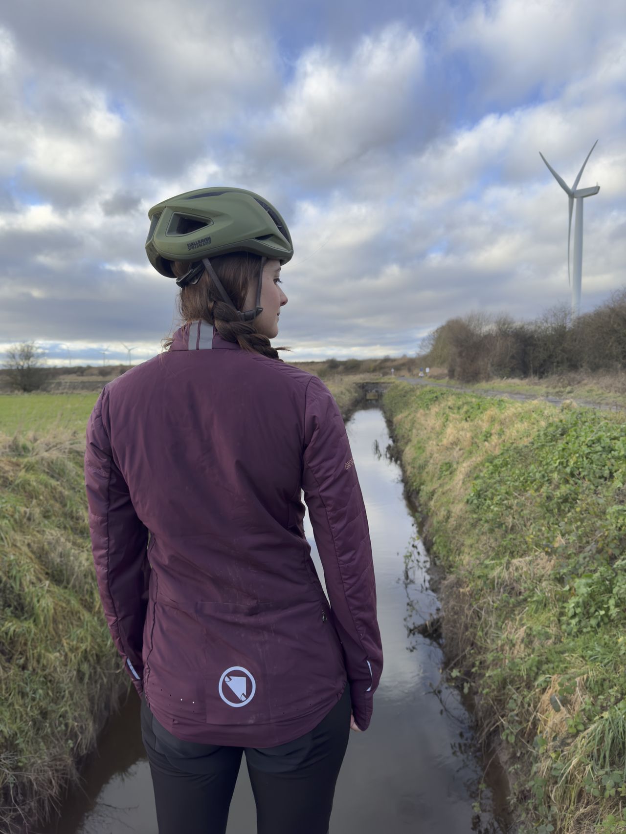 Reverse of burgundy Endura jacket, woman stands in front of a stream wearing a green helmet