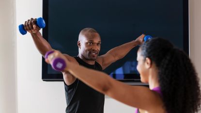 Man and woman working out in front of TV with dumbbells