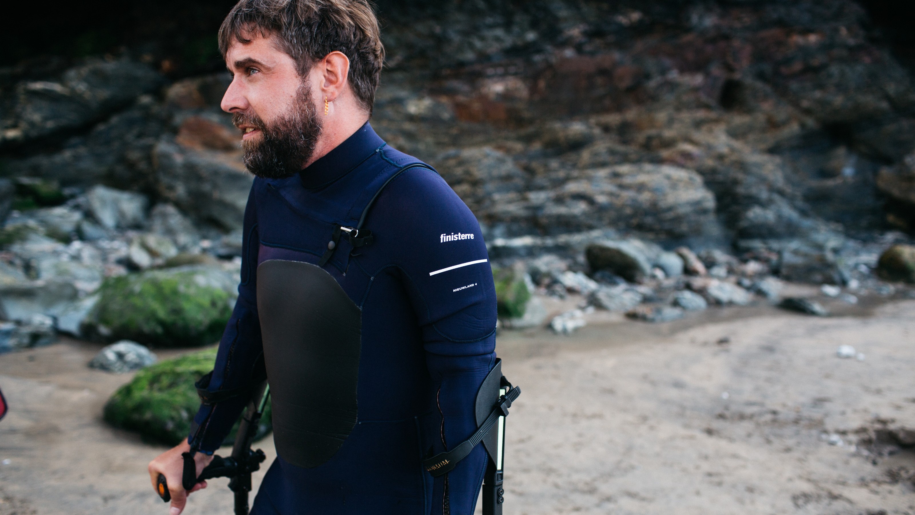 A man using cruches at the beach wearing an adaptive Yulex wetsuit with Finisterre logo