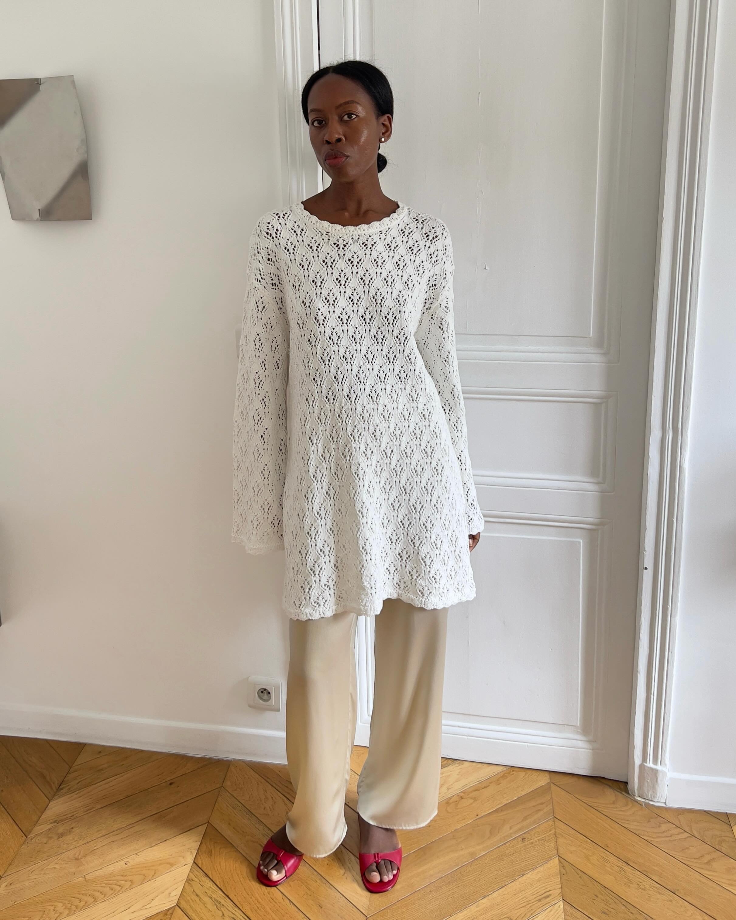 Influencer Sylvie Mus wearing a white crochet dress, beige satin trousers and red mule sandals.