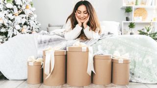 A woman with long dark hair lies on her stomach looking at a pile of beautifully wrapped Christmas gifts tied with white bows
