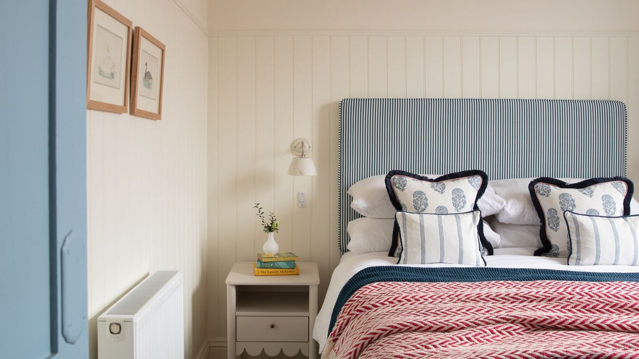 bedroom with white panelled walls, blue striped headboard, red throw on bed