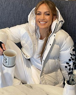 Jennifer Lopez smiling in a white Super Puff jacket with a hood.