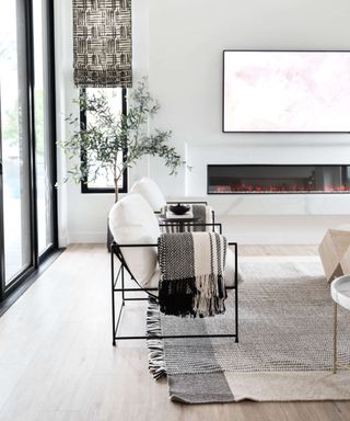 white modern living room with metal and upholstered armchairs, monochromatic scheme, modern fireplace, blind, crittall doors, rug, hardwood floor