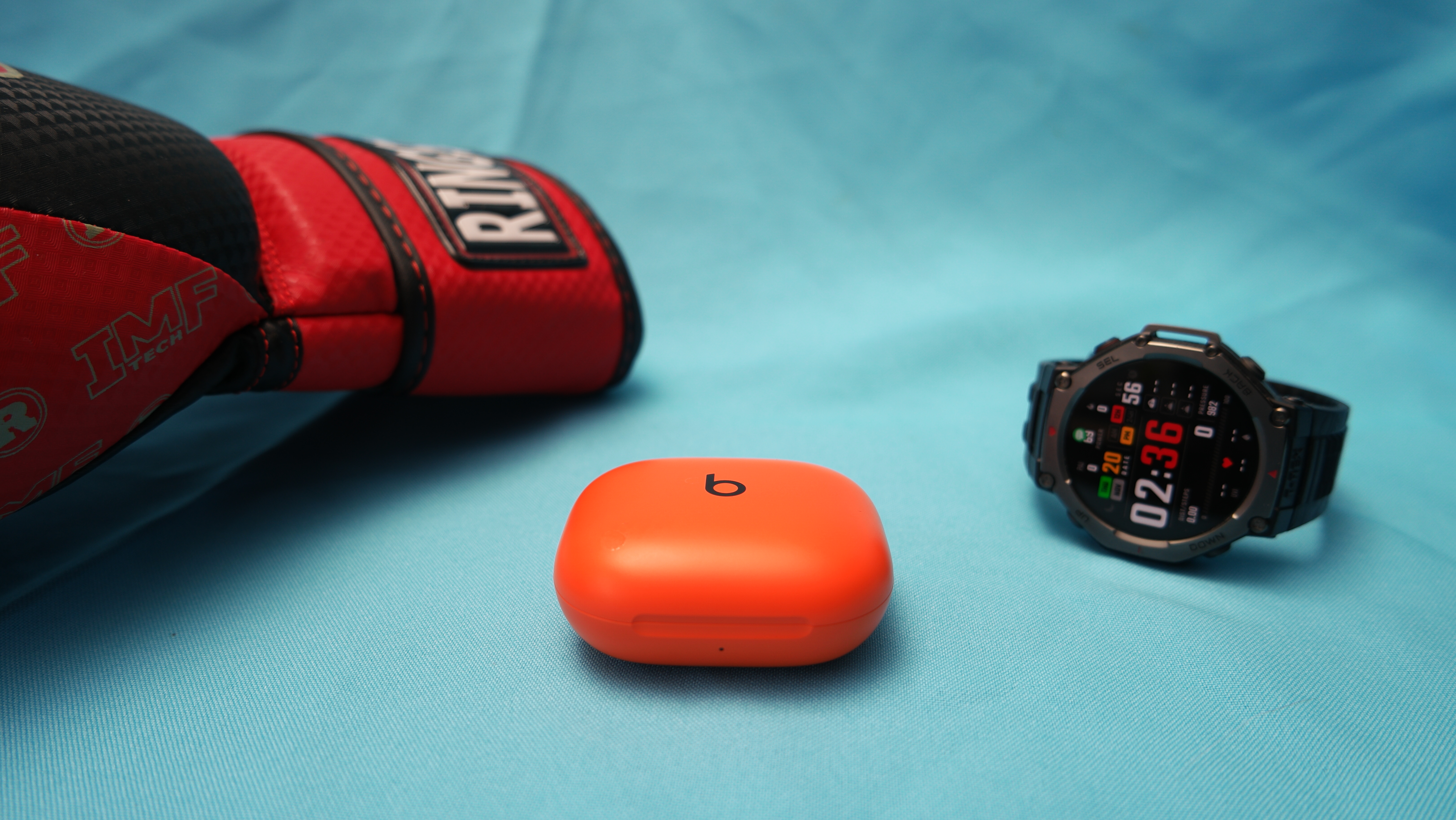 Beats Powerbeats Fit on a table with a boxing glove and Amazfit T-Rex behind it