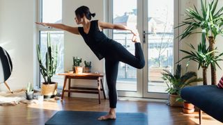 Woman practicing strength training and yoga on yoga mat in front room surrounded by healthy plants