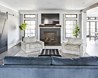 A living room with a blue velvet sofa, black barn doors and a brick and black marble fireplace