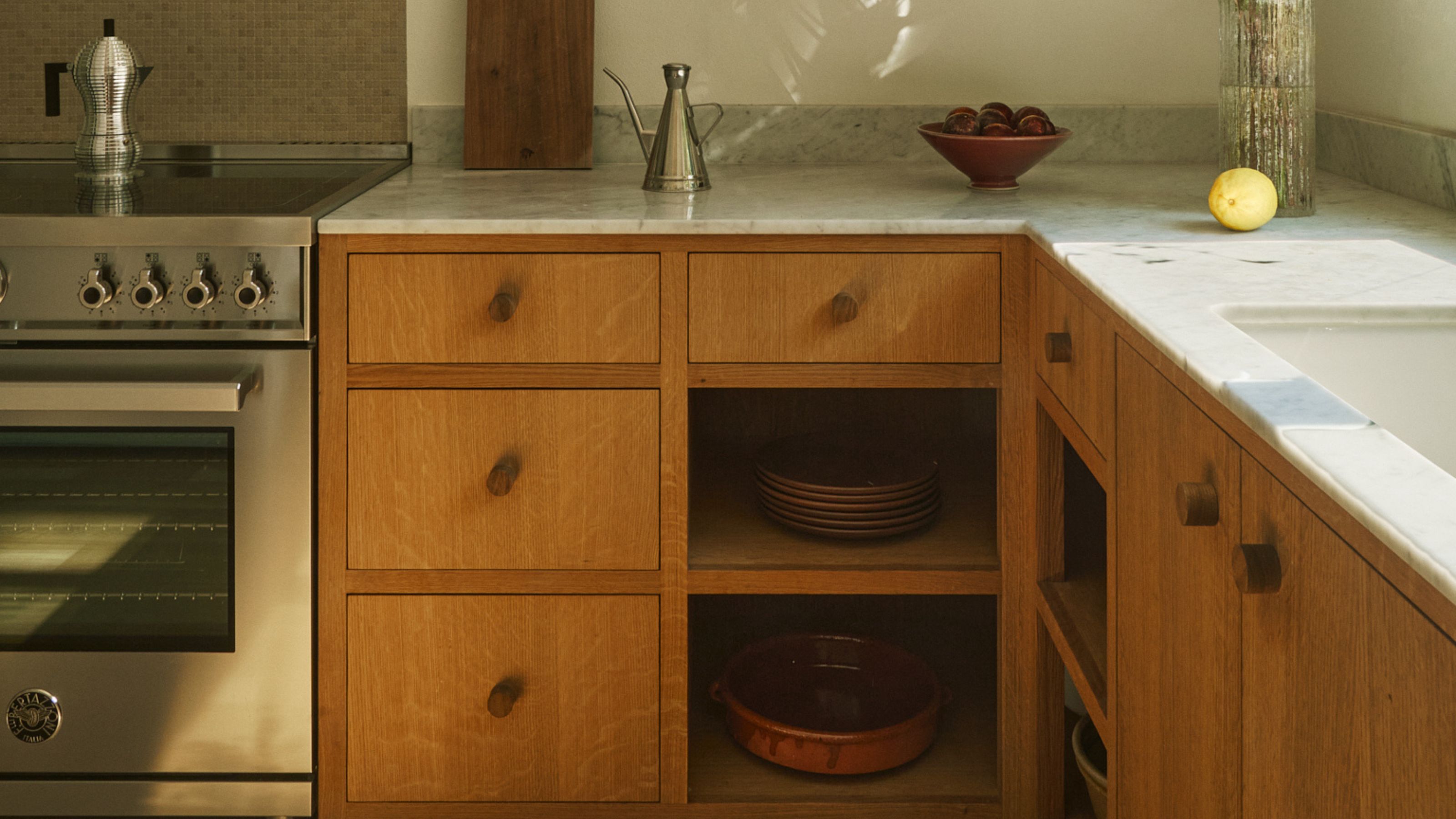 A kitchen with an open corner shelf with dishes and kitchen essentials. There is also a view of the countertop, stove as well as oven 