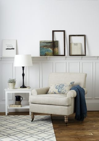 white living room with panelling and shelf, armchair, wooden floor, side table, table lamp