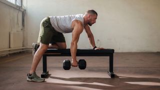 Man in starting position for one-arm dumbbell arc row