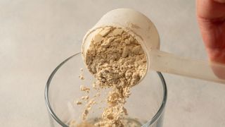 protein powder being poured out of a scoop and into a glass