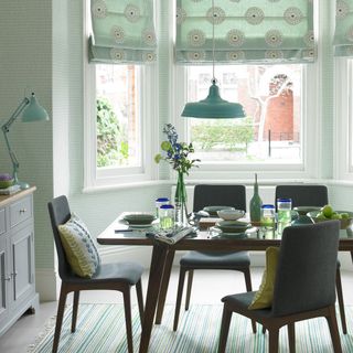 A green dining room with wallpaper and patterned blinds