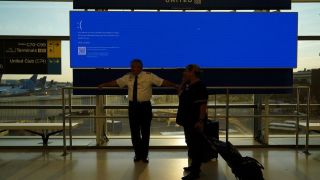 United Airlines employees wait by a departures monitor displaying a blue error screen