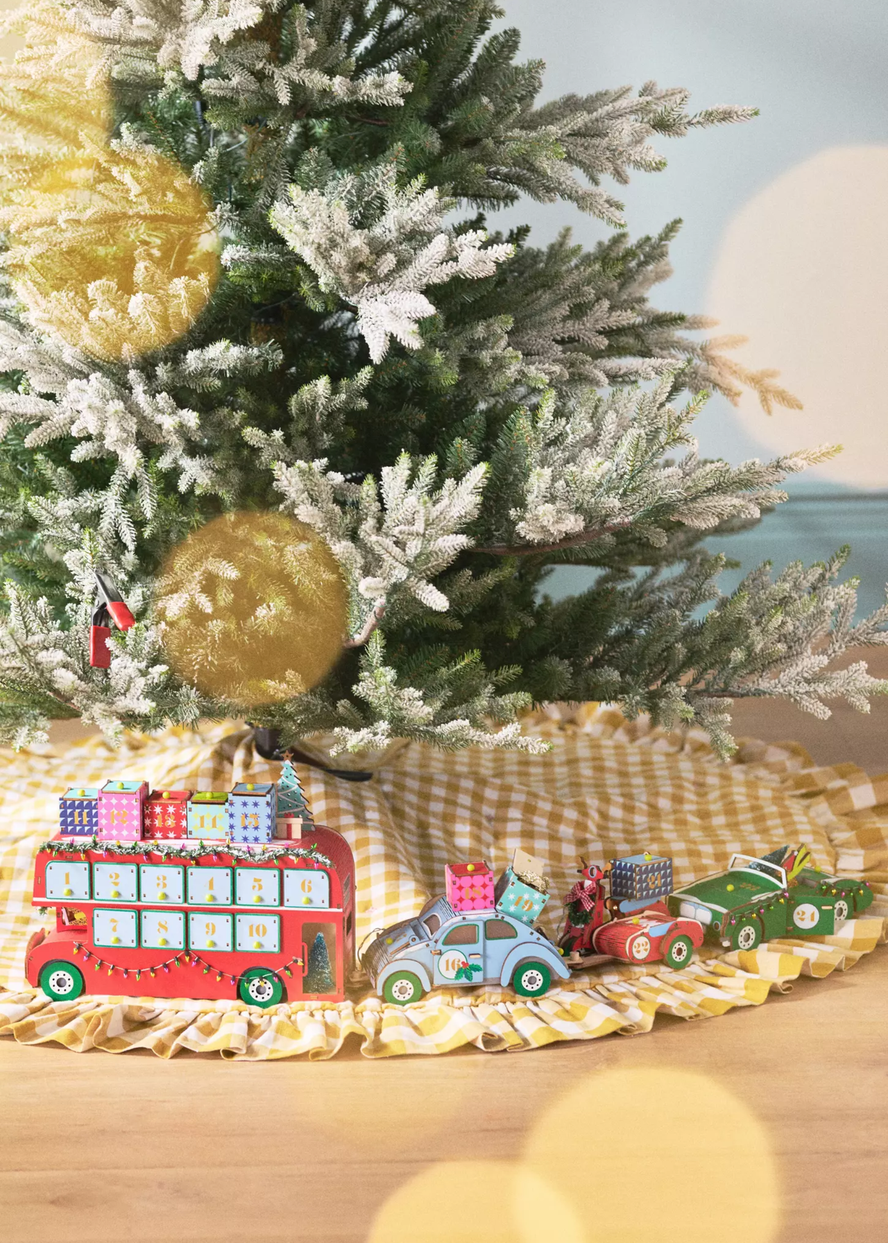 anthropologie advent calendar which is a red london bus and each piece builds cars as part of a travel collection with presents on top - these are styled around the yellow checkerboard skirt of a frosted christmas tree