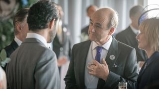 David Haig in grey morning dress as Archie Glover-Morgan talks to a man in a suit as Victoria Dalton (Jane Horrocks) looks on in COBRA: Rebellion.