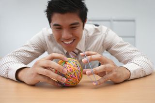 Businessman making a colourful elastic rubber band ball at office desk, smiling
