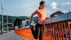 Woman stretching thigh muscle standing on bridge looking at view, smiling, representing stretches for runners