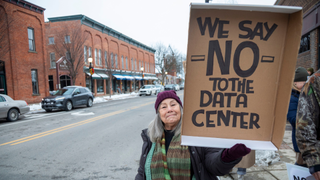 a protester holding up a sign against a data center