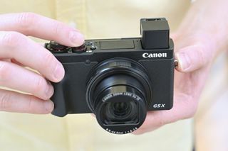 Kameraet Canon G5X Mark II holdes i to hender med søkeren åpen.