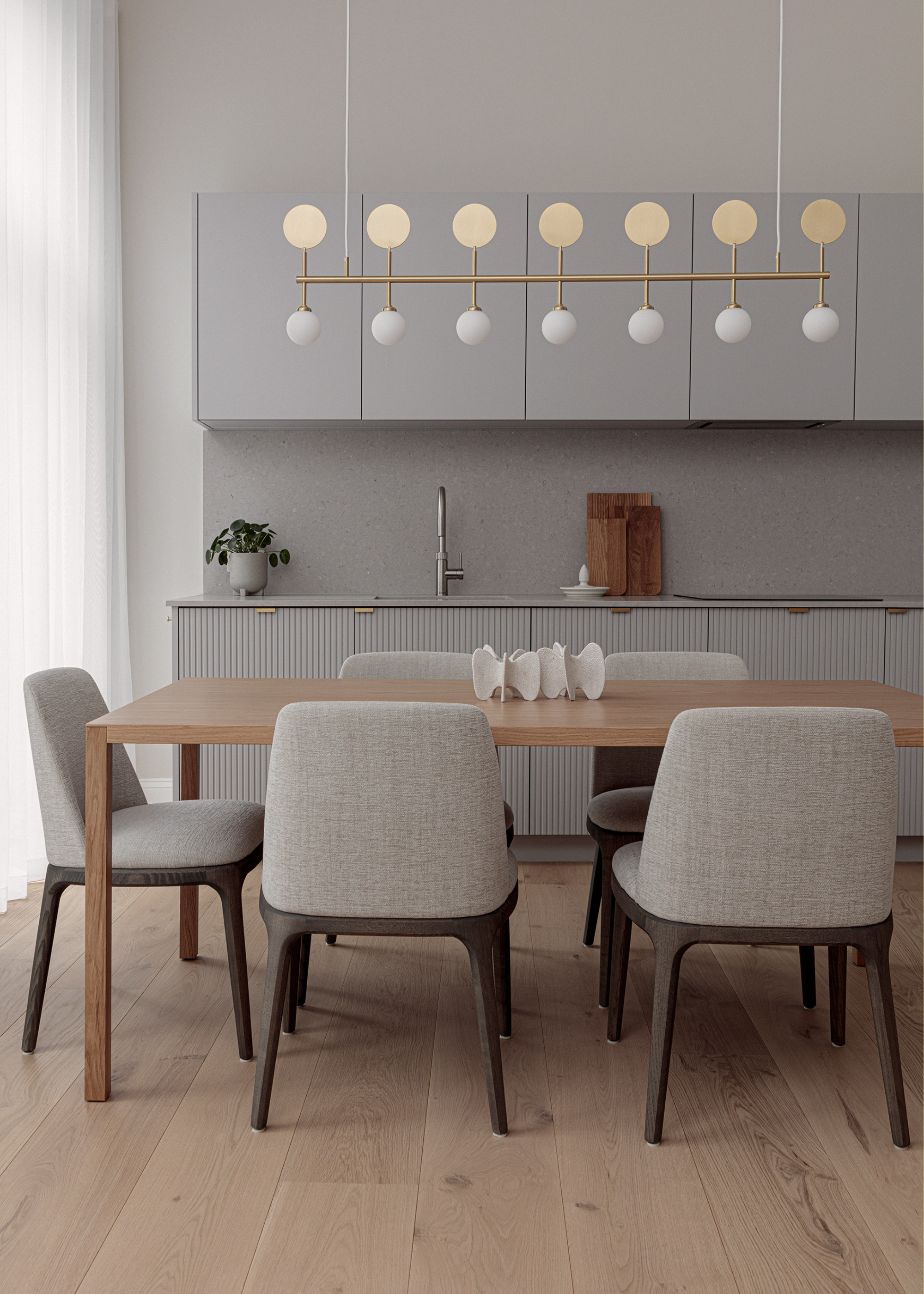 A kitchen and dining room with gray cabinets, a wood dining table, matching gray chairs, and a statement gold and exposed bulb light