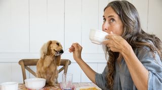 Woman feeding dog at table